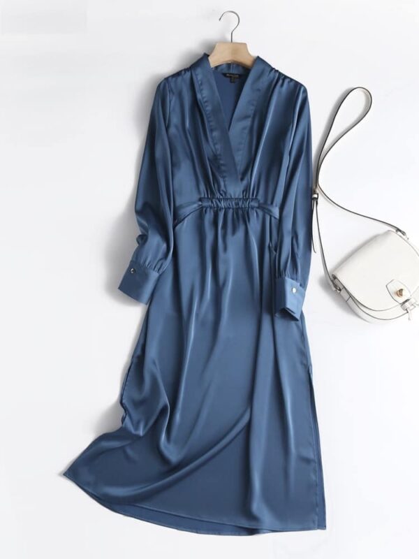 0-657c7Robe en satin à manches longues bleu d'été. La robe est posée sur un fond blanc à côté d'un sac à main blanc en cuir.