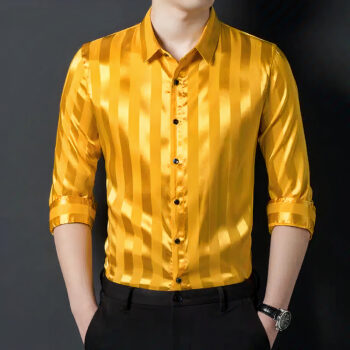 Homme portant une chemise jaune en satin avec des rayures, les manches 3/4, les mains dans les poches du pantalon noir, fond gris foncé.