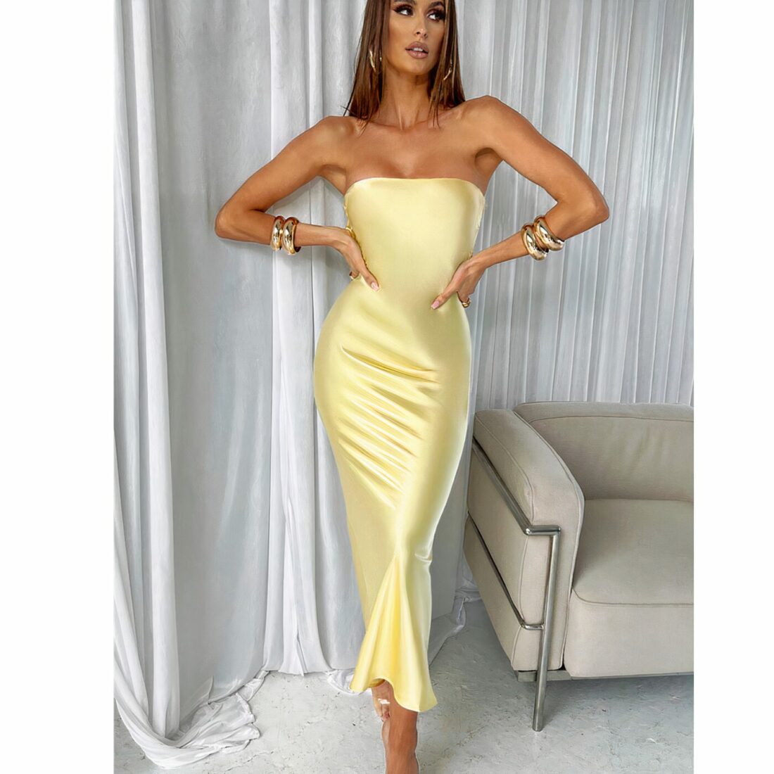 Une femme debout à côté d'un canapé en robe longue en satin jaune