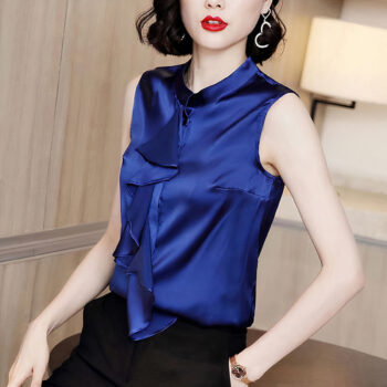 Femme portant une une chemise sans manches en satin à volant bleu électrique. Femme de type asiatique assise sur un bureau, sa main gauche dans sa poche.