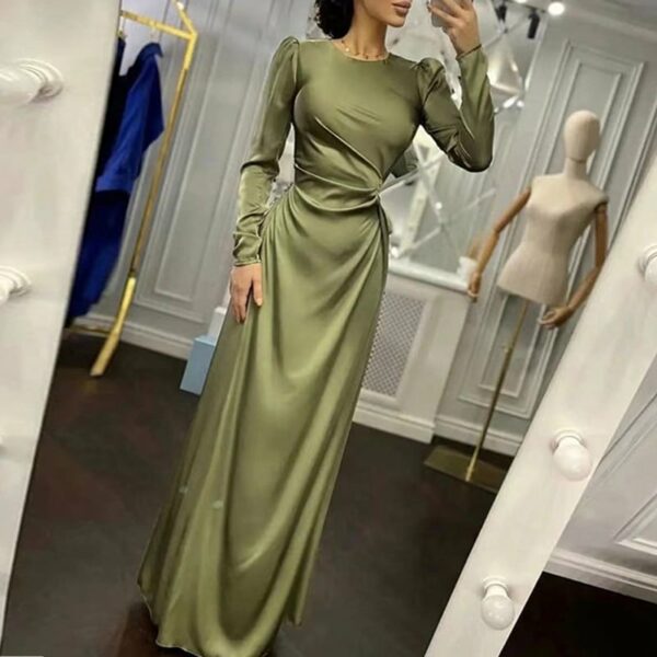 Femme portant une robe de soirée élégante à manches longues en satin et verte. La femme se prend en photo dans un miroir. La scène se passe dans une salle d'essayage.