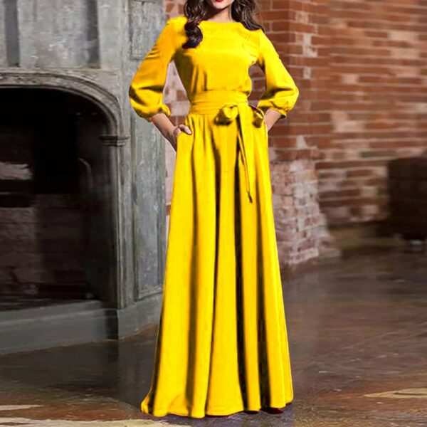 Femme portant une belle robe longue en satin jaune. La robe est à manches longues. La femme pose devant une grande cheminée dans un grand salon de château.
