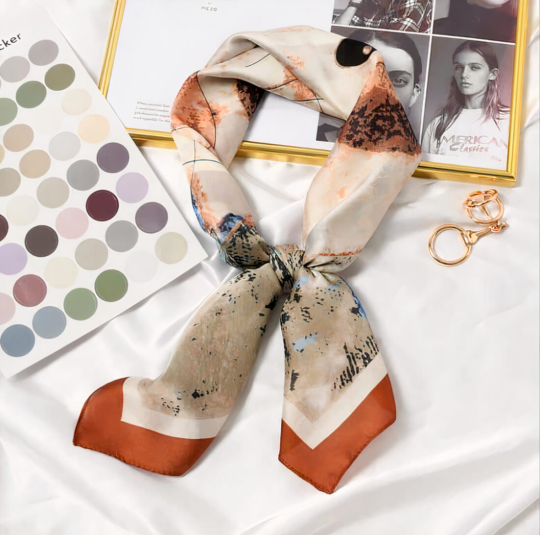 Foulard en satin noué, posé sur un tissu en satin blanc et un magazine avec un nuancier