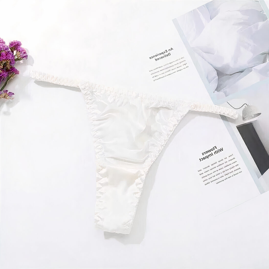 string blanc élastique posé sur un fond blanc avec fleur violette en haut à gauche et page de catalogue à droite.