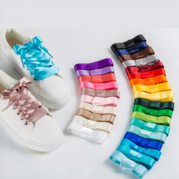 Une paire de chaussures blanche est posée avec des lacets de deux couleurs différentes ( une bleu et l'autre rose ) . On voit sur la droite, un ensemble de lacets de différentes couleurs.