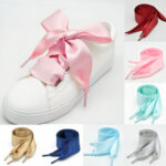 Chaussure blanche avec un lacet rose. On voit en bas et à droite de l'image, différentes couleurs de lacets.