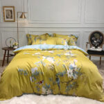 Lit avec des draps jaunes aux motifs de fleurs et d'oiseaux dans une chambre avec du parquet, des fleurs blanches et un miroir rond au mur