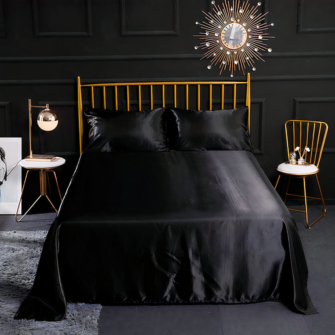 Drap en satin noir sur un lit double avec 2 coussins assortis, tête de lit barreaux dorés avec chaise à droite assortie et table de chevet à gauche, un tapis gris à gauche du lit. mur noir et miroir en forme de soleil au dessus du lit.