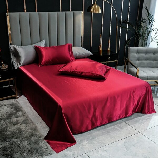 On voit un lit doouble paré de draps en satin rouge foncé. La tête de lit est gris foncé.