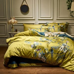 Lit avec des draps jaunes aux motifs de fleurs et d'oiseaux dans une chambre avec du parquet, des fleurs blanches et un miroir rond au mur