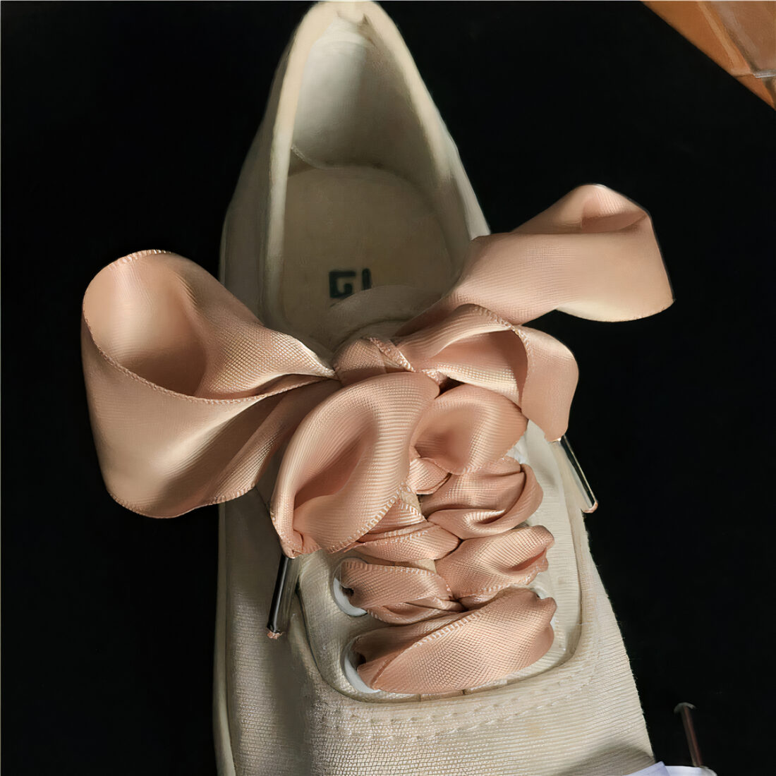 Chaussure blanche avec lacets rose poudrée, fond noir.