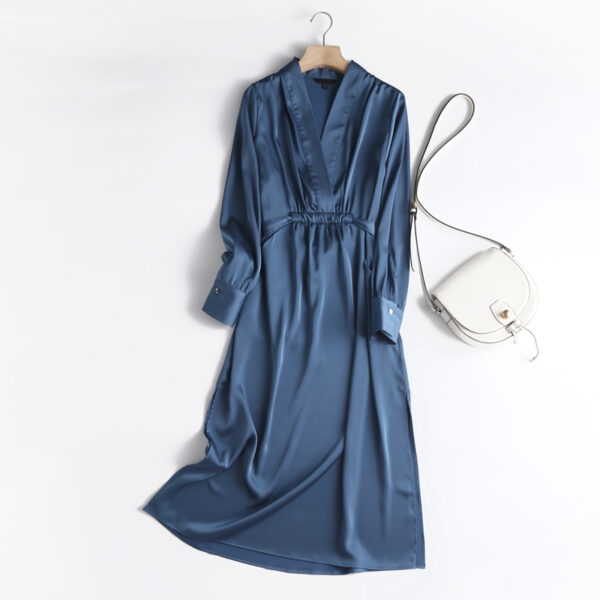 Robe en satin à manches longues bleu d'été. La robe est posée sur un fond blanc à côté d'un sac à main blanc en cuir.