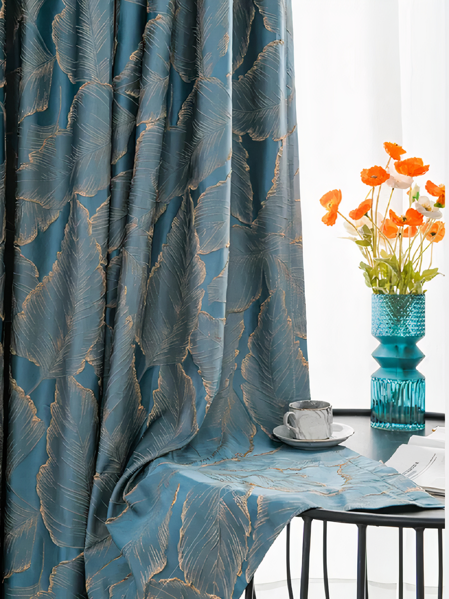 Rideau bleu avec des motifs dorés posé sur une table basse avec un vase et des fleurs posé sur la table ainsi qu'une tasse de café posé sur le rideau