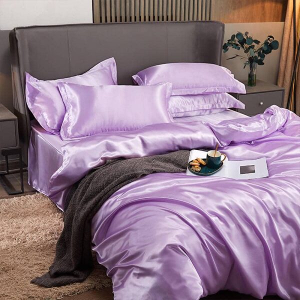 Lit avec des draps violets en satin avec un plaid marron par dessus. Moquette beige au sol et vas avec des fleurs posé à côté du lit.