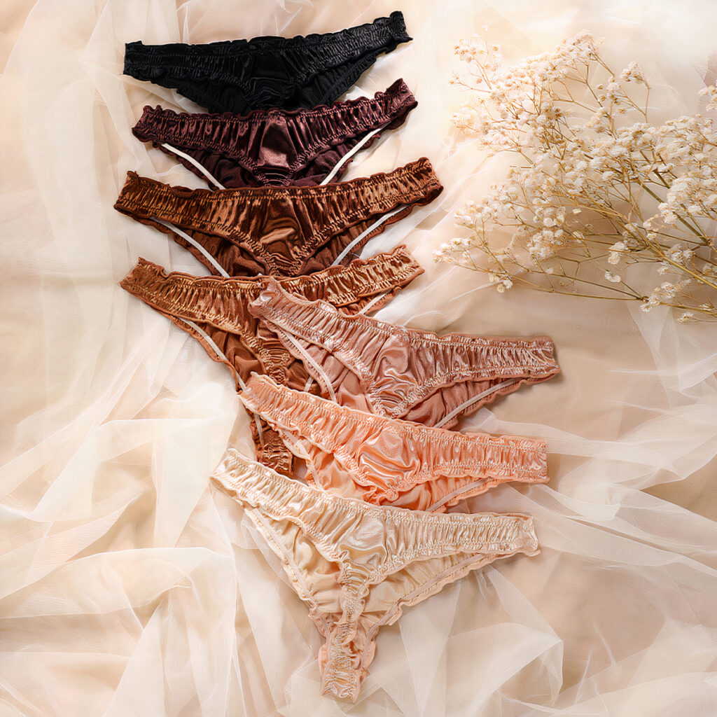 Plusieurs strings de couleurs différentes du noir au beige en passant par différentes teintes de marron posés sur un tissu beige.
