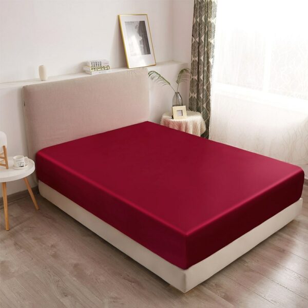 On voit un lit deux places dans une chambre moderne et lumineuses. Le matelas est paré d'un drap housse en satin rouge.