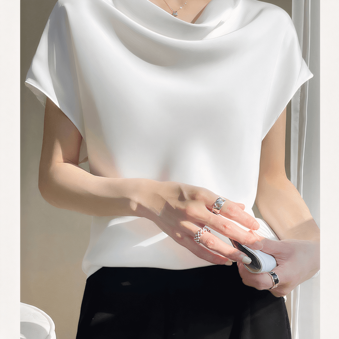 on voit une femme qui porte un T-shirt en satin blanc avec un décolleté drapé et un pantalon noir