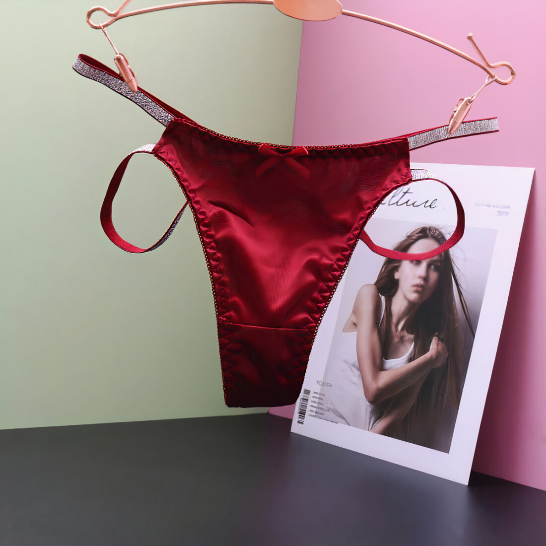 String rouge en satin accroché sur un contre orange, dans un angle avec des murs rose et gris. Le sol est noir. On voit aussi, une photo.