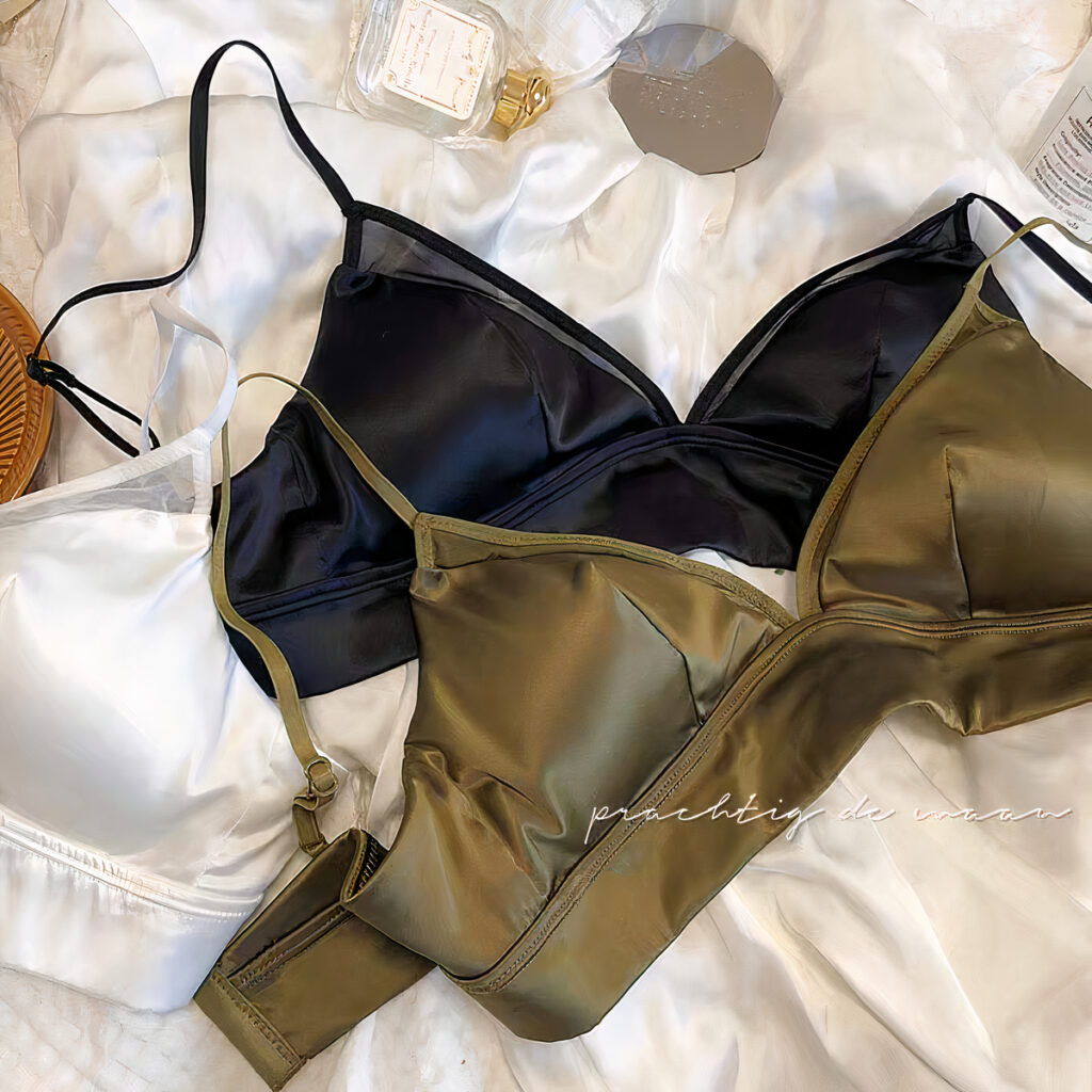 3 soutien gorges de couleur différentes, blanc, noir et vert posés sur un drap clair. un flacon de parfum vide à côté.
