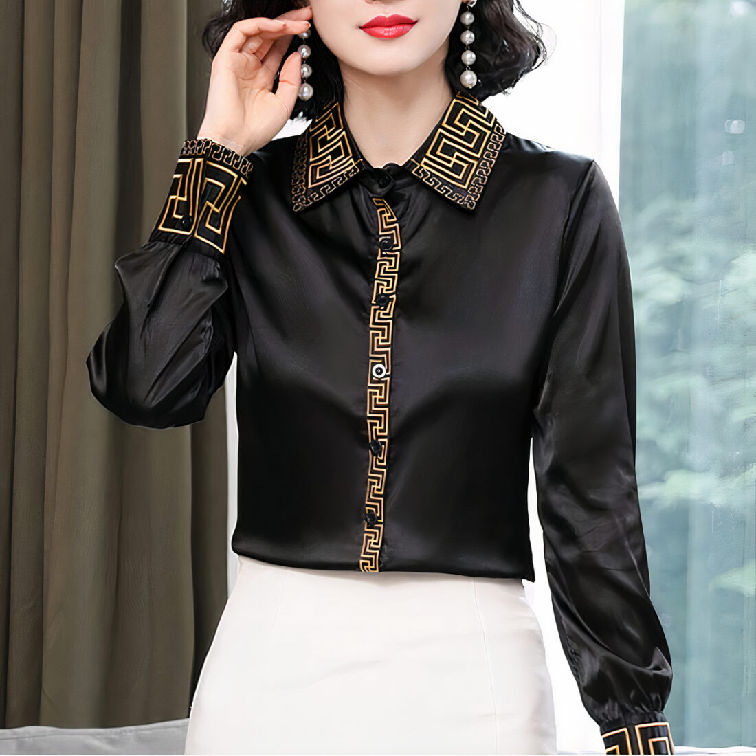 Une femme portant une chemise en satin noir manche longue avec des motifs dorés sur le col , les manches et les boutons.