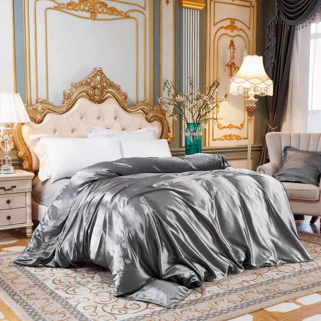 Lit avec des draps argentés en satin dans une chambre avec un tapis, une table de chevet, une lampe, un vase vert avec des fleurs dedans.