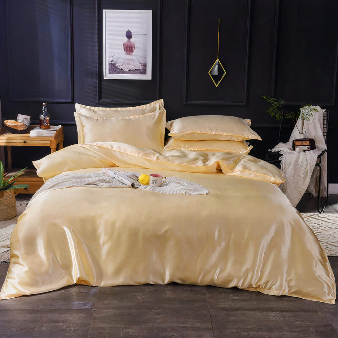 Photo d'un lit avec des draps de satin beige. 4 coussins assortis. un mur noir avec un cadre blanc. une table de chevet de chaque côté avec des objets dessus.
