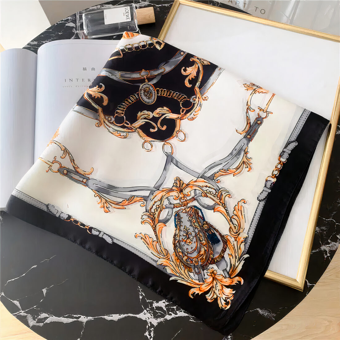 Foulard en satin noir et blanc style vintage élégant. LE foulard est plié en triangle, posé sur une table en marbre noir.