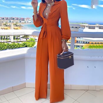 femme métisse portant une combinaison manches longues orange, boutons ouverts sur la poitrine. Elle est sur un balcon et tient un vanity dans sa main gauche.