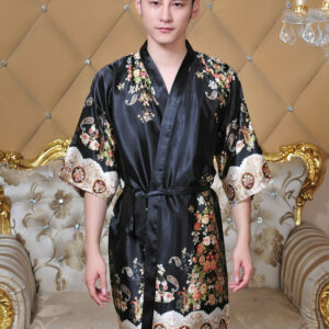 Homme portant un kimono noir avec des fleurs. Fond marron avec un canapé.