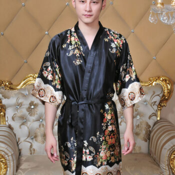 Homme portant un kimono noir avec des fleurs. Fond marron avec un canapé.