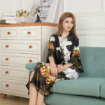 Une femme assise dans un canapé vert et vêtue d'un kimono en satin noir avec des motifs