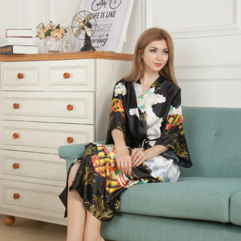 Une femme assise dans un canapé vert et vêtue d'un kimono en satin noir avec des motifs