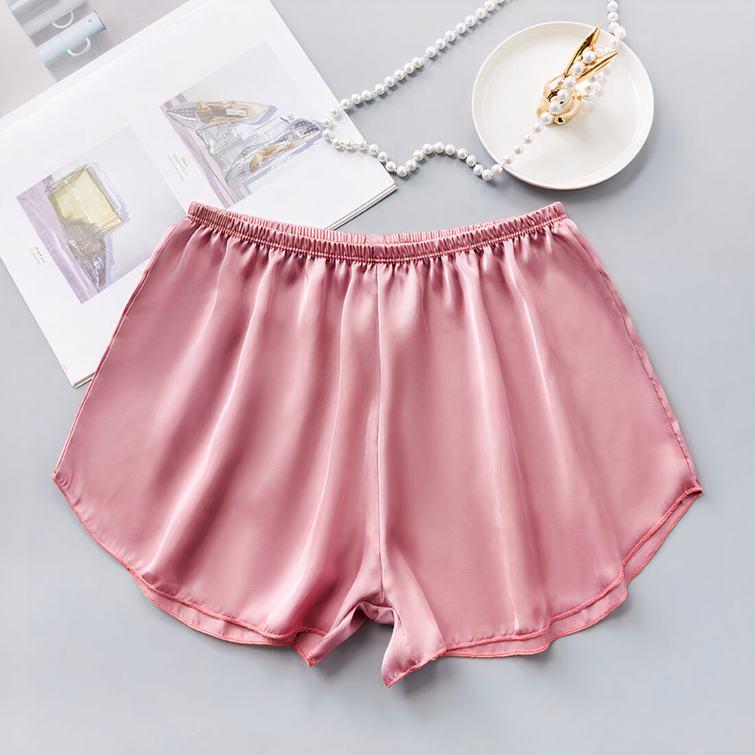 short en satin rose taille élastique. Il est bien présentés et il y a un porte bijoux et un collier en perles à côté.