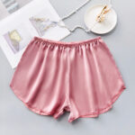 short en satin rose taille élastique. Il est bien présentés et il y a un porte bijoux et un collier en perles à côté.