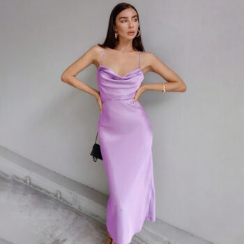 Robe longue à col bénitier mauve à bretelles fines portée par une femme debout, les cheveux bruns et les mains sur les hanches.