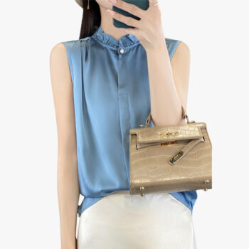 Blouse en satin bleu à manches courtes portée par une jeune femme brune qui fait un selfie avec son téléphone, sur fond blanc.