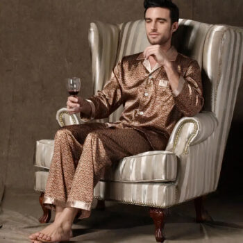 Homme assis dans un fauteuil, un verre de vin à la main, portant un pyjama en satin marron et pieds nus.