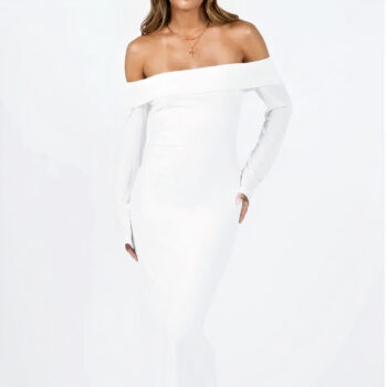 robe de mariée blanche longue à manches longues avec épaules dénudées portée par une femme aux cheveux mi-longs. Son bras est le long de son corps, sa main gauche est posée sur sa hanche. sa jambe gauche est légèrement en avant.