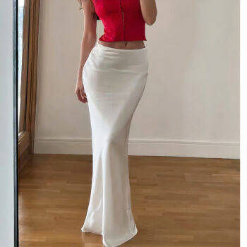 Jupe longue slim de couleur blanche portée par une femme debout avec un haut moulant rouge. Le sol est un parquet et le mur derrière est blanc.