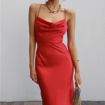 Femme portant une robe longue rouge en satin à bretelles fines et à col bénitier, un sac dans sa main gauche sur fond gris.