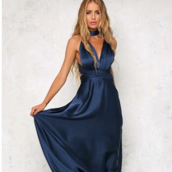 Une femme blonde qui porte une robe longue en satin bleu nuit et qui la relève avec sa main droite