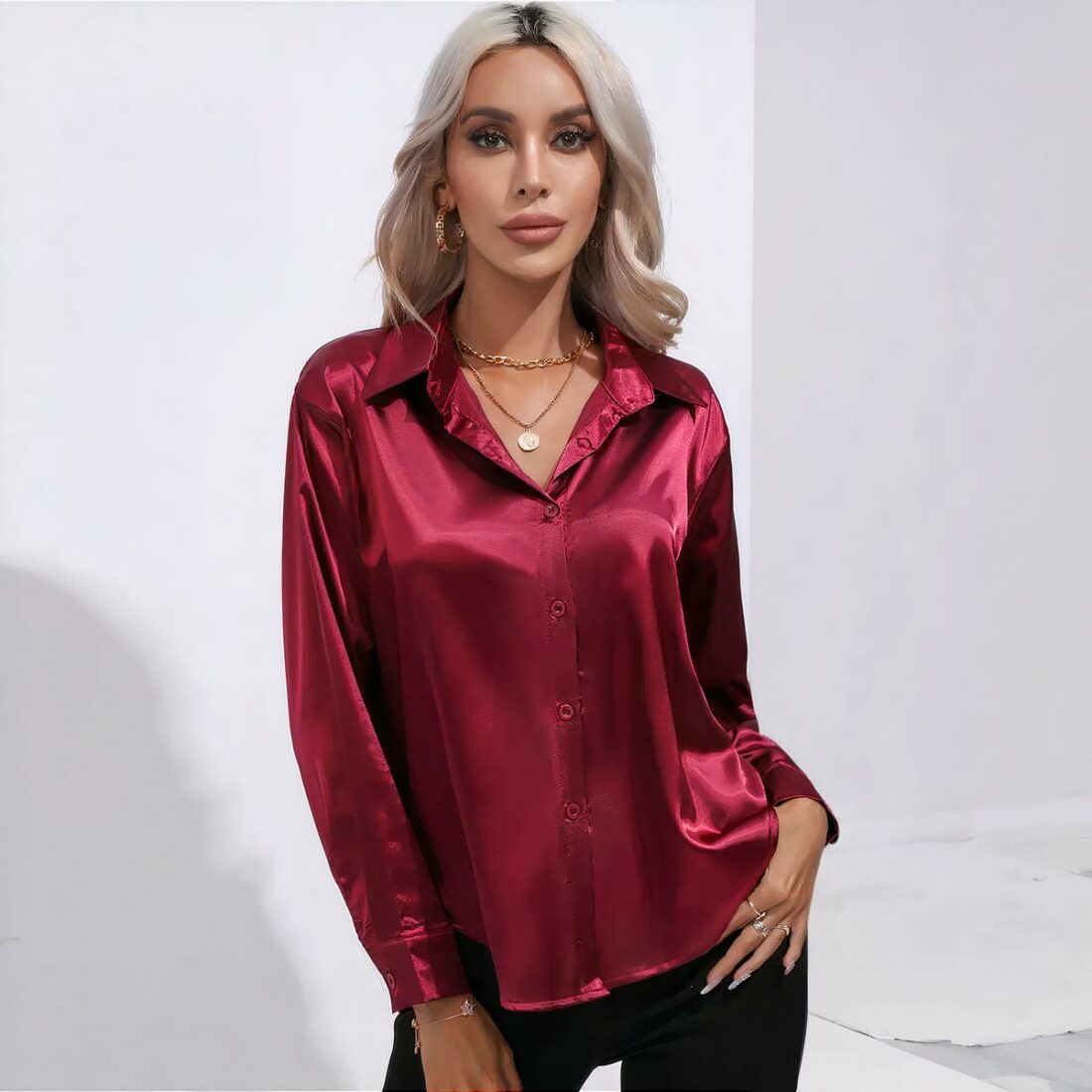 chemise rouge en satin portée par une femme blonde aux cheveux détachés, elle porte un pantalon noir et sa main gauche est posée sur sa hanche.