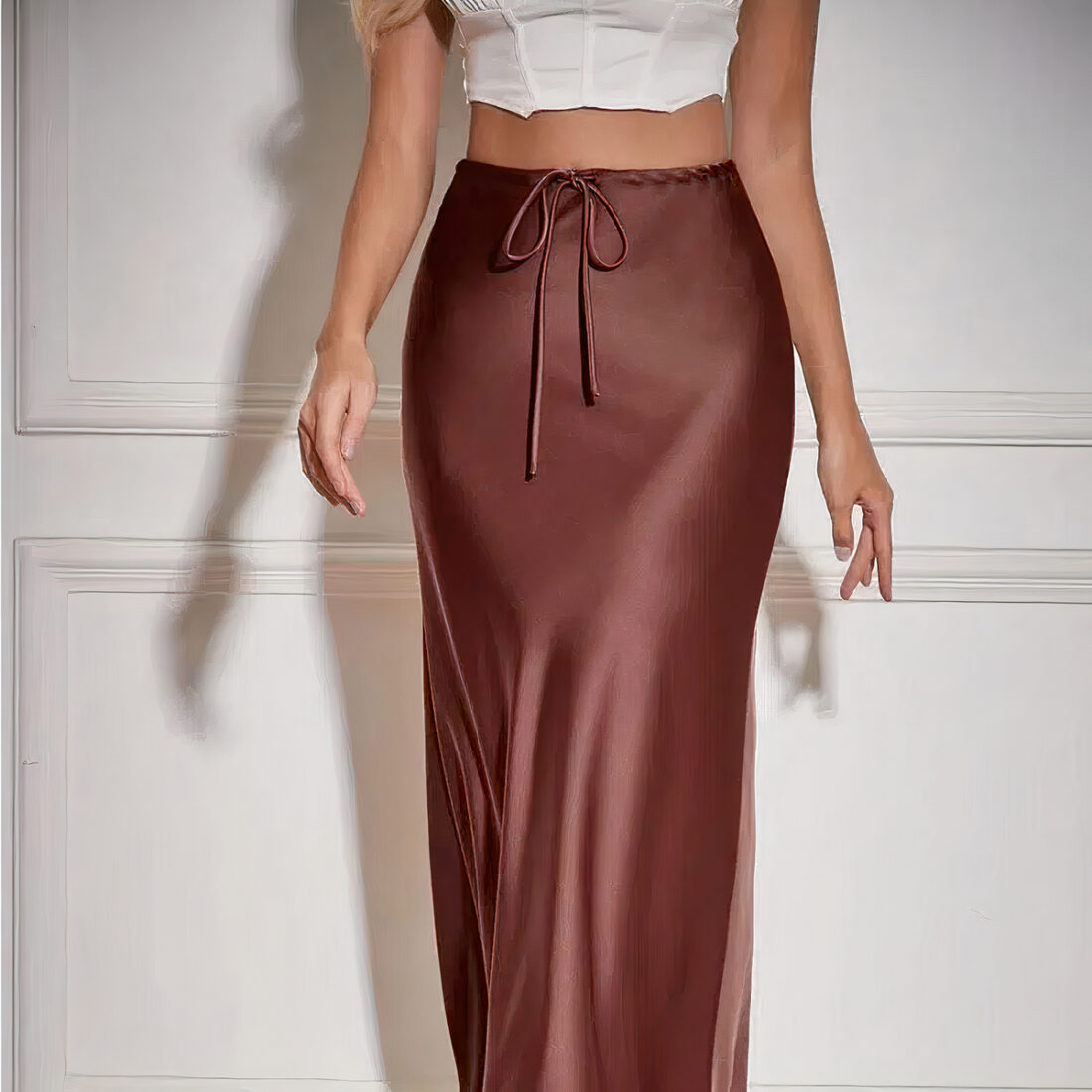 une jupe longue marron portée par une femme debout. Les bras le long de son corps et elle porte un haut moulant blanc laissant apparaître son ventre.