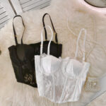 2 soutiens gorge bustier en satin et dentelle posés l'un sur l'autre, le blanc sur le noir. Ils sont de face posés sur un tissu poilu beige.