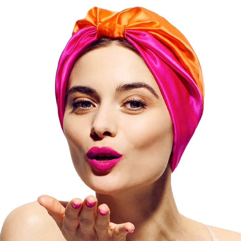 Femme maquillée portant un bonnet bicolore orange et rose, sa main droite paume vers le haut devant elle.