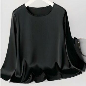 Haut noir à manches longues en satin posé sur un cintre avec un sa à main gris à droite.