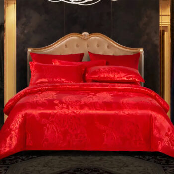 Lit 2 places avec literie rouge en satin et jacquard. 4 coussins assortis. Tête de lit marron. Le mur est noir, tapis gris devant le lit.